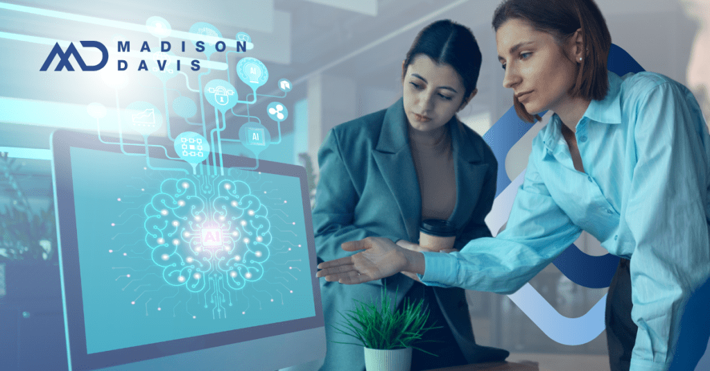 Two women in corporate attire view a computer monitor with a 2D digital brain labeled "AI"